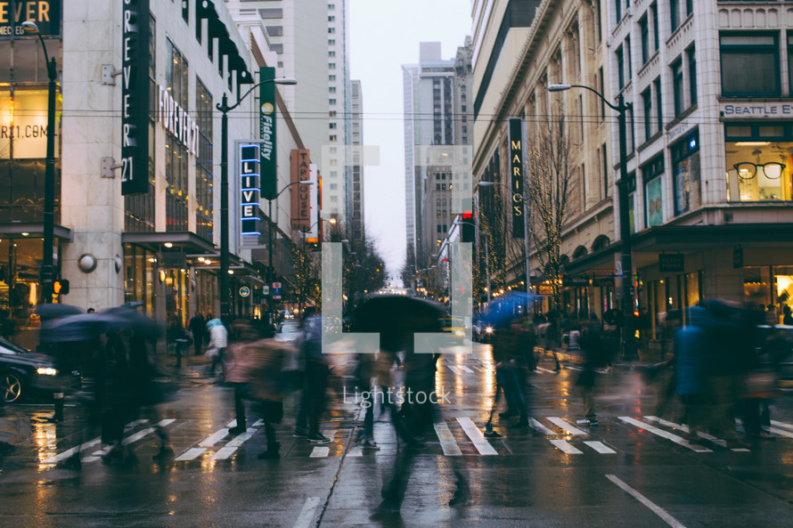People with umbrellas walk across a rainy city street.