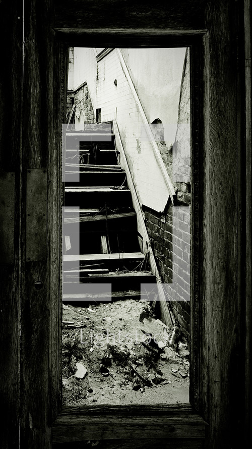 Broken wooden staircase seen through door frame.