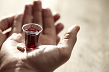 A communion cup and wafer in the palm of a hand