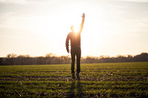 silhouette of a man jumping in a field with his hand raised to God glowing under sunlight