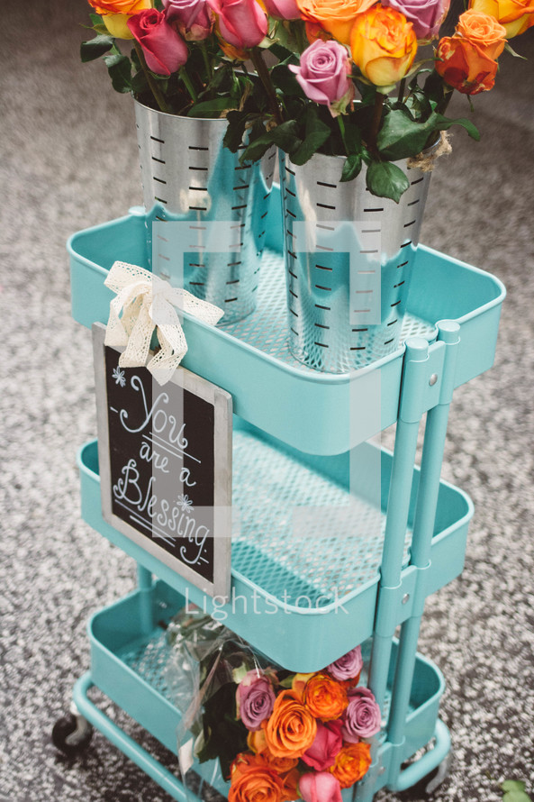 A blue metal cart with bouquets of flowers and a sign reading, "You are a Blessing."