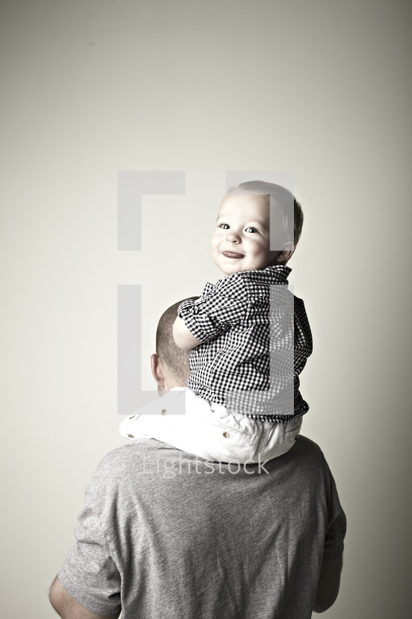 A young son sits on his father's shoulders