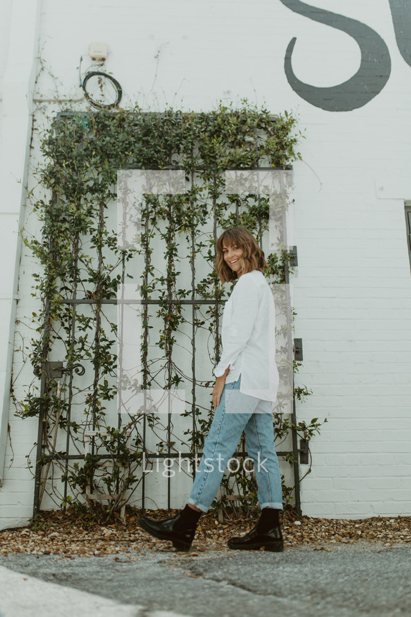 a woman in boots standing in front of vines on a gate 