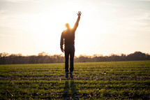 silhouette of a man jumping in a field with his hand raised to God