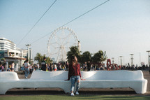 a woman sitting on a bench with a ferris wheel in the background 