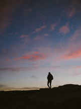 silhouette of a person walking on a mountaintop at sunset 
