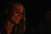 woman's smiling face sitting by a campfire 