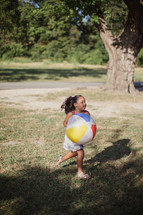 A little girl running outdoors with a beach ball.