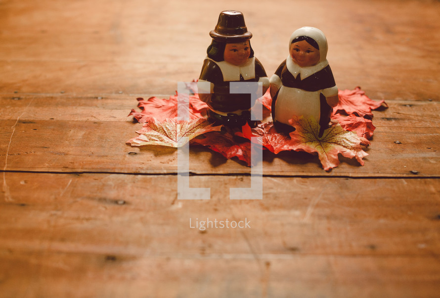 Pilgrim figurines on fall leaves on a wooden table -- Thanksgiving decor.