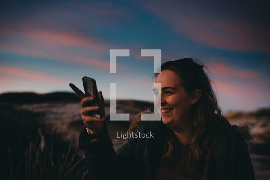 woman holding a cellphone taking a picture at sunset 