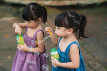 toddler girls blowing bubbles outdoors 