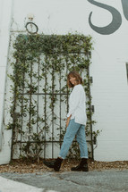 a woman in boots standing in front of vines on a gate 