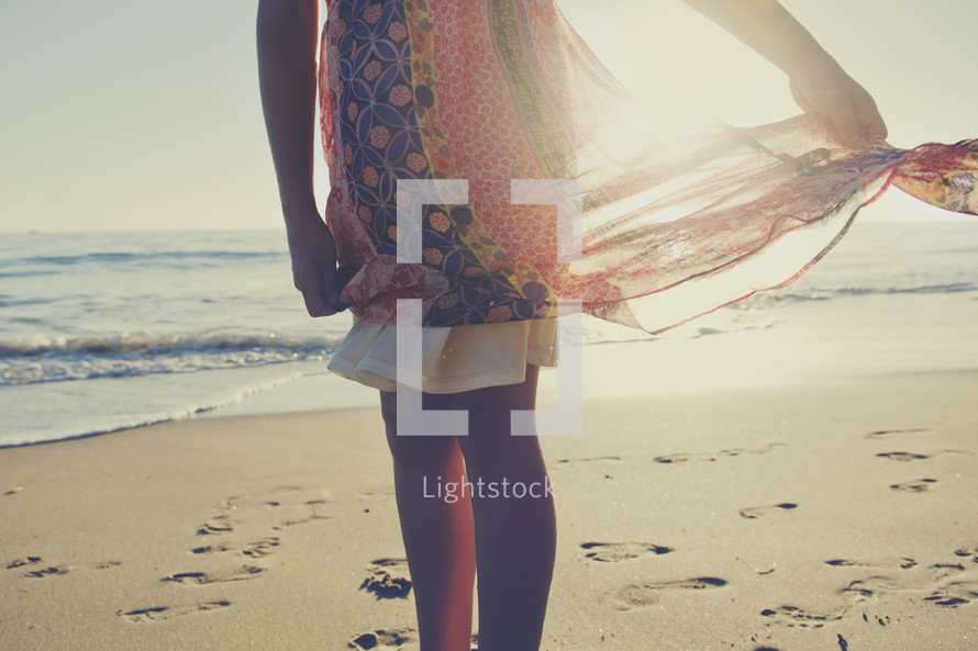 a woman standing on a beach holding her dress in the sunlight 