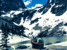 couple sitting in front of a mountain lake 