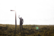 a man praying in front of a cross with a raised hand 