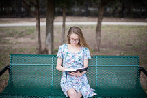 young woman reading a Bible on a bench 