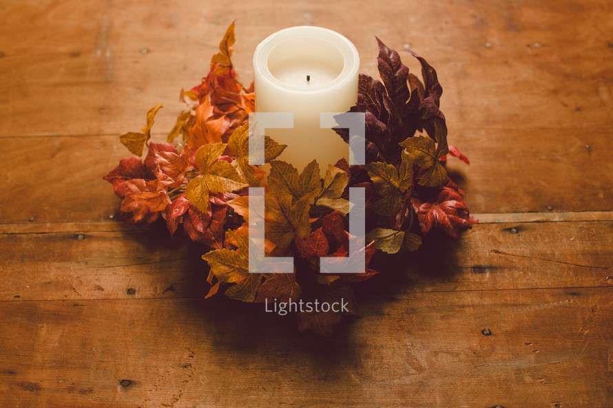 Candle with a wreath of fall leaves on a wooden table -- Thanksgiving decor.