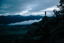 a man standing at the edge of a cliff at dusk 