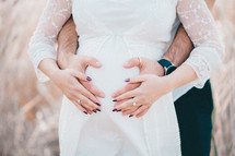 Hands of future parents - unrecognizable man and woman on pregnant belly background.
