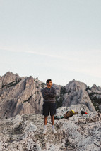 a man with camping gear standing along on a rocky mountaintop 