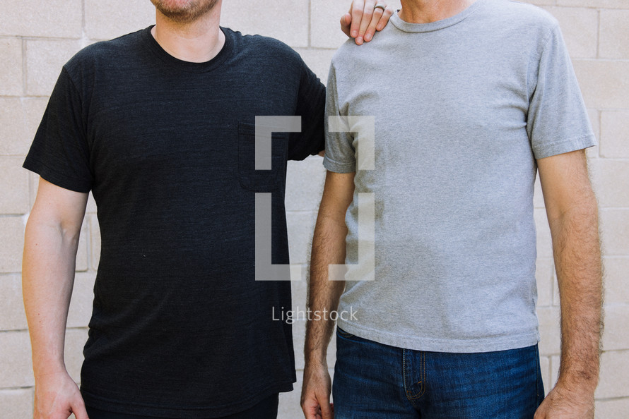 Torso view of two men standing side by side. One is wearing a black pocket tshirt and the other a gray tshirt.