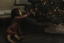 a toddler girl touching a Christmas tree 