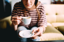A woman on a coach drinking coffee from a white coffee cup.
