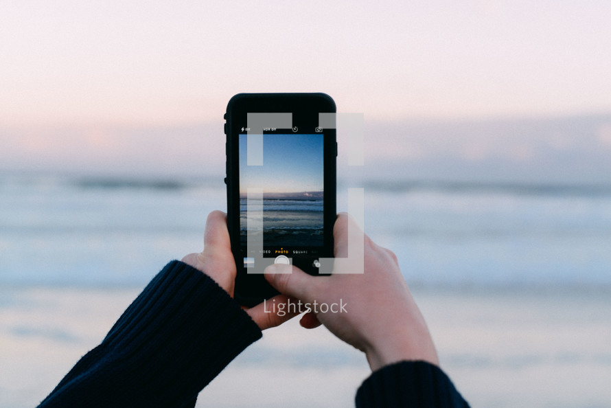 Taking a picture of the ocean with a cell phone.