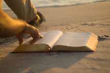man pointing to scripture in the Bible sitting on a beach 