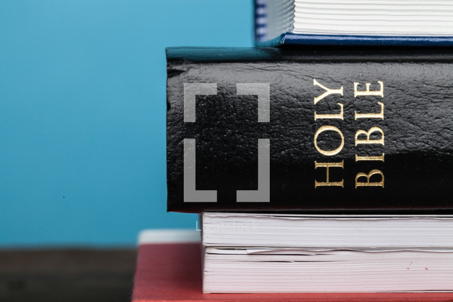 A Bible in the middle of a stack of books.