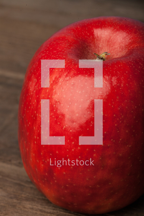 A bright red apple on a wooden surface.