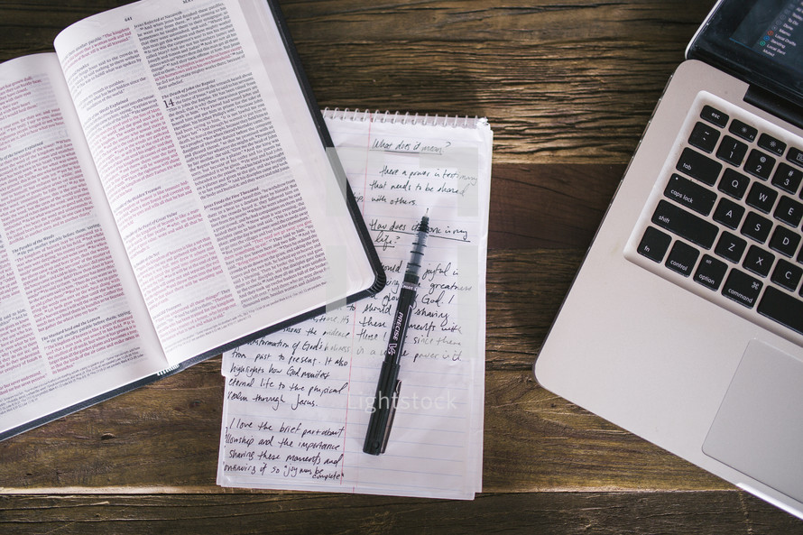 open Bible and notes on a notepad and pen and laptop 
