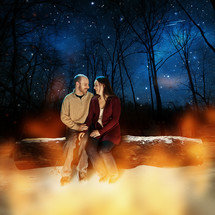 A man and woman sitting on a log at night 