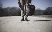 a man standing on a gravel road holding a map and backpack 