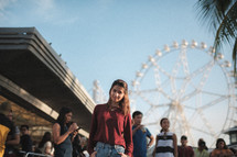 a woman standing in a crowd with a ferris wheel in the background 