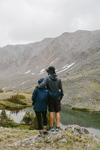 people standing near a lake surrounded by mountains 