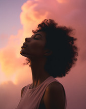 A young woman looking with eyes closed head lifted toward sky during sunset