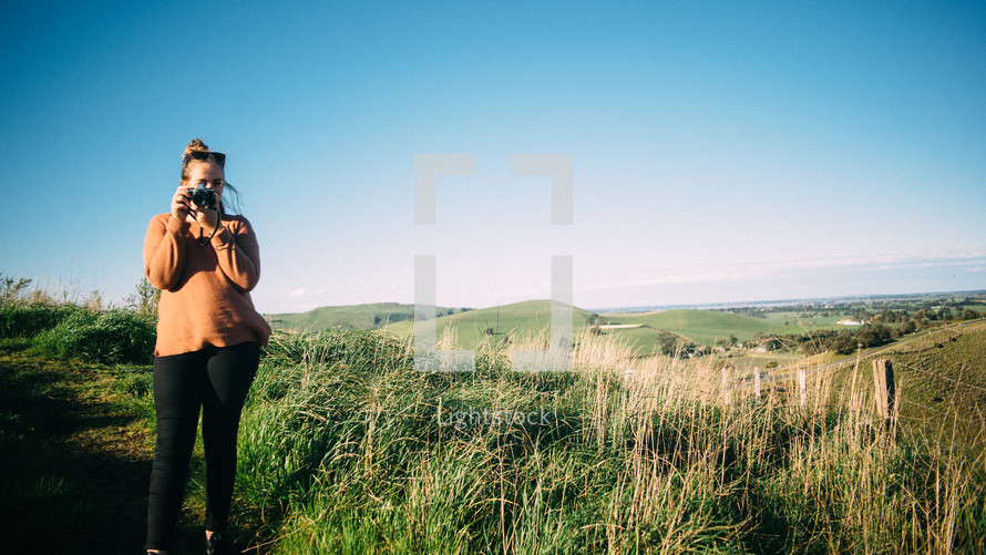 a woman standing on a hill holding a camera 