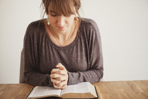 woman with her hands folded in prayer on a Bible
