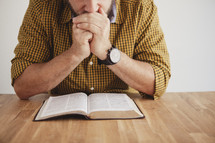 man reading a Bible with his hands folded in prayer