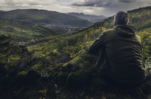 a man sitting on a mountain top taking in the view 