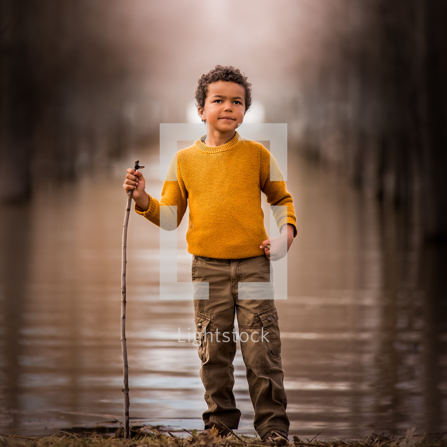 a child standing beside a pond holding a stick 
