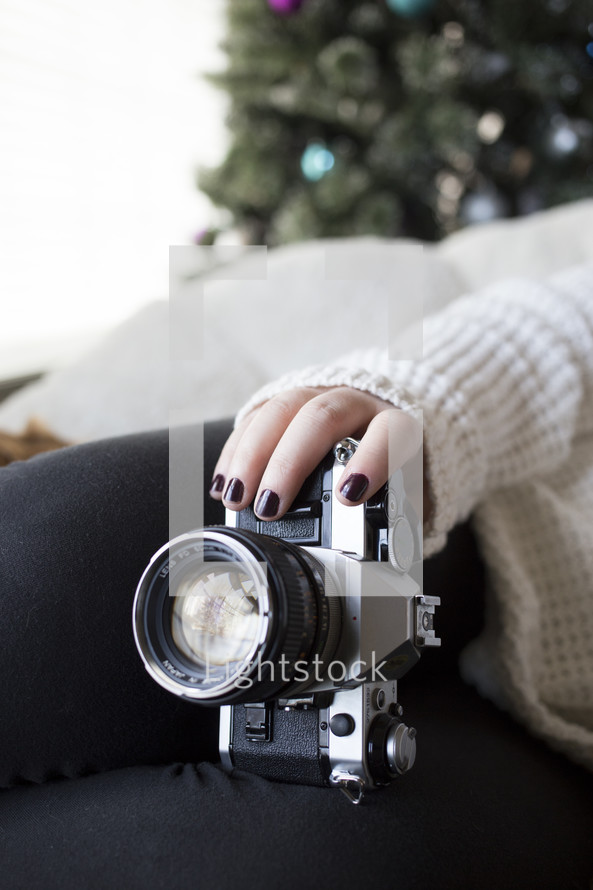 a woman holding a camera on her lap with a Christmas tree in the background 