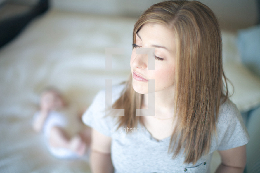 Woman with eyes closed and infant daughter in the bed in the background.