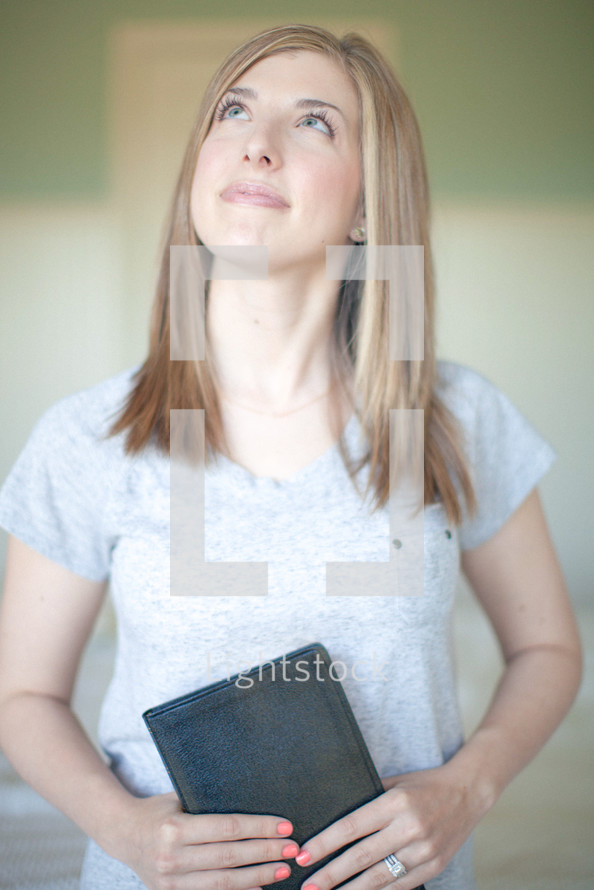 Woman holding a Bible looking up to God.
