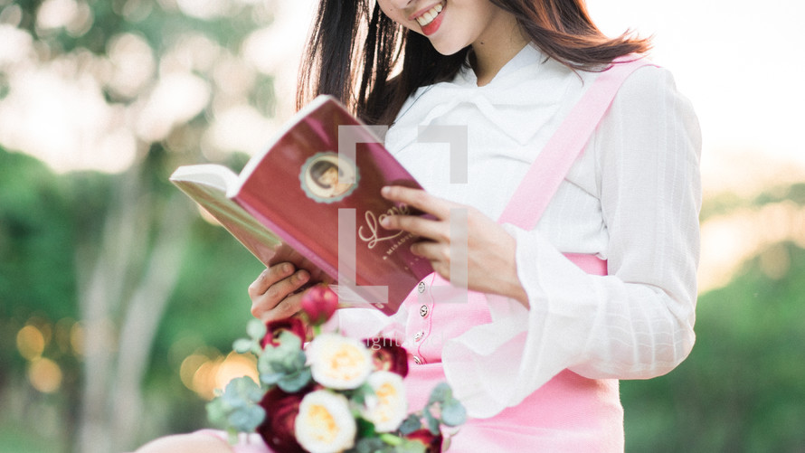 a woman sitting in the grass with a bouquet of flowers in her lap reading a love book