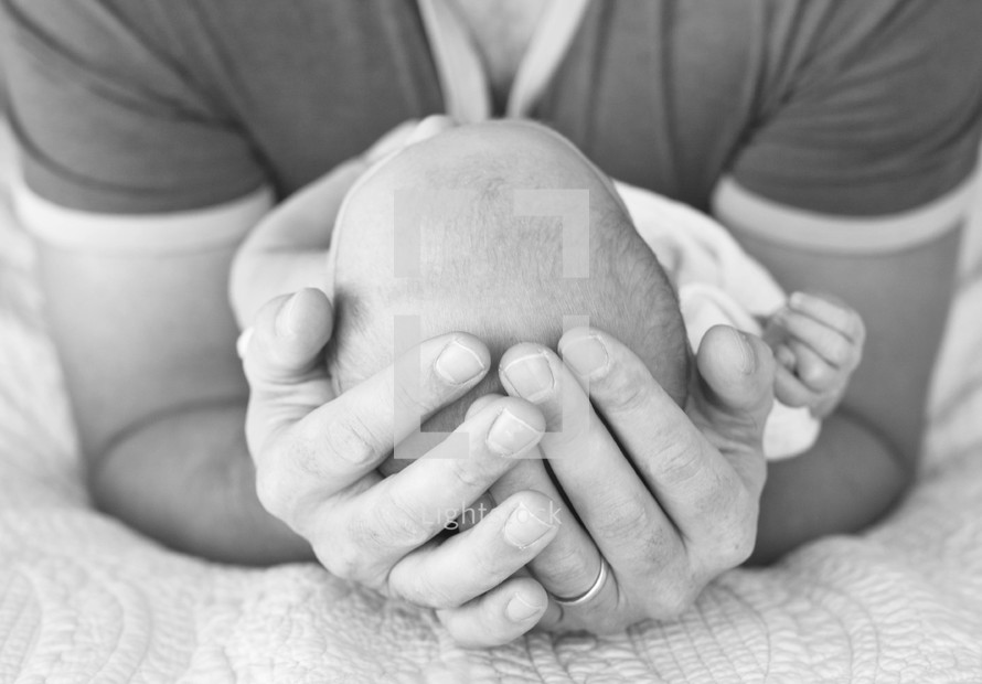 A father cradling an infant in his hands. 