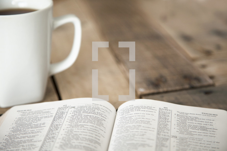 pages of an open Bible and coffee mug on a wood table 