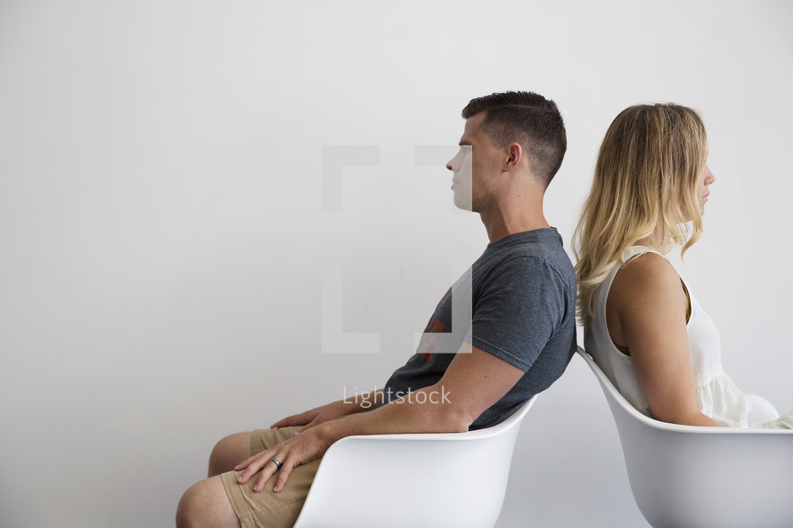 a couple sitting in chairs back to back 