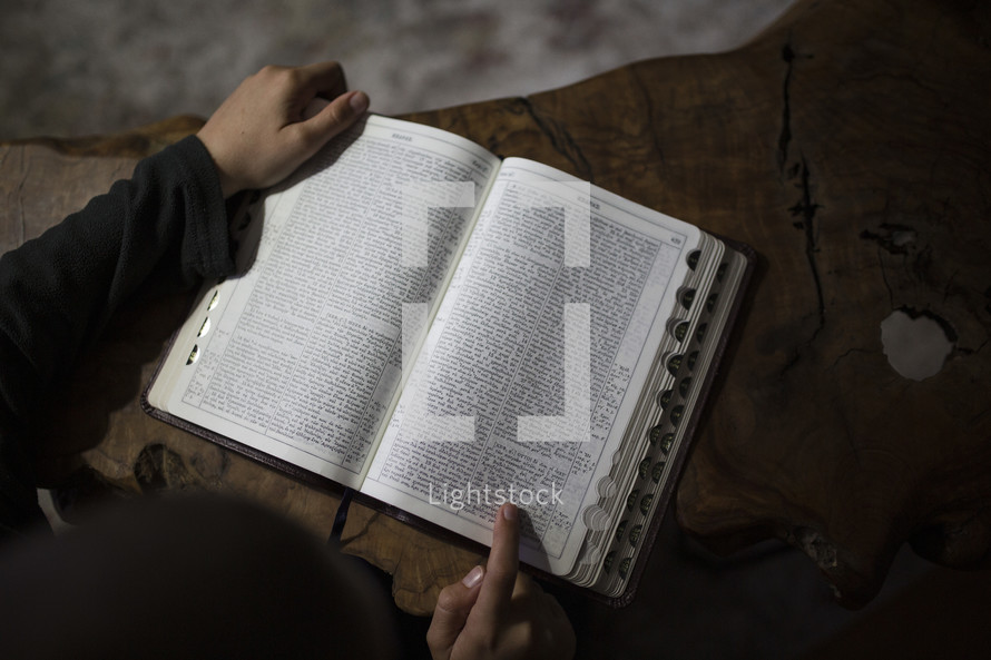 Little boy reading the Bible at a table.